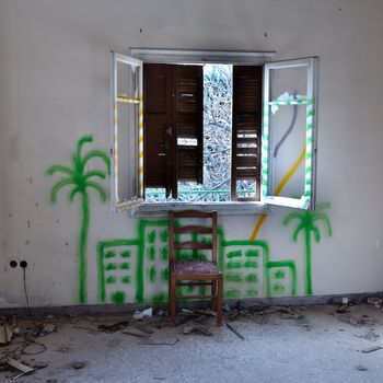 Chair and broken window in abandoned interior. City graffiti on the wall.