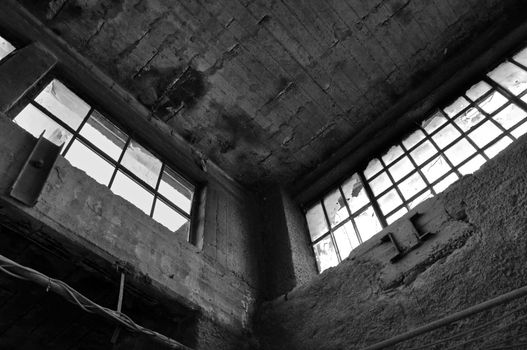 Broken windows concrete wall and ceiling in derelict factory. Black and white.