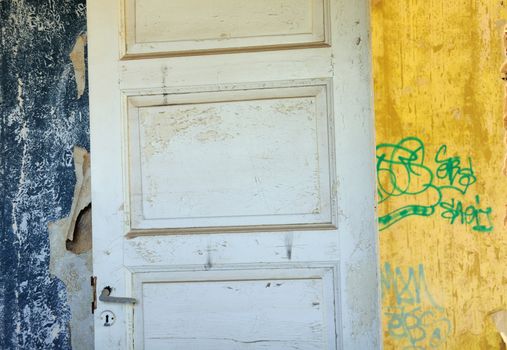 Wooden door, torn vintage wallpaper and peeling walls in abandoned interior.