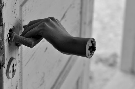 Detached doll hand pulling old door handle in haunted house.