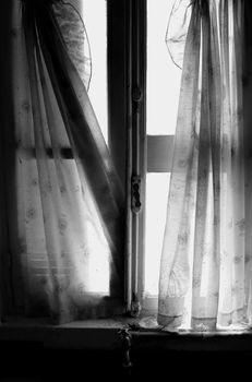 Ragged window curtains in abandoned house. Black and white.