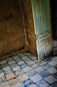 Decayed room interior old door tiled floor and roots growing on crumbling brick wall.