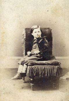 Portrait of Victorian young boy on chair. Sourced from antique cabinet card vintage photograph created by A.D. Lewis, Newcastle on Tyne, UK, circa 1870.