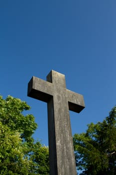 A christian carved stone cross with trees and a blue sky.