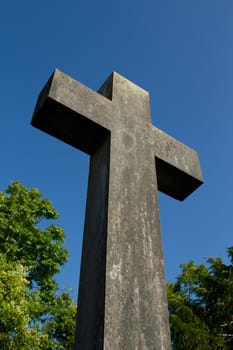A christian carved stone cross with trees and a blue sky.