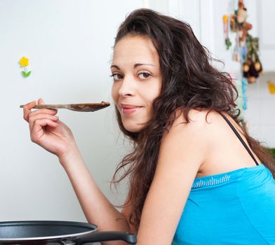 Nice brunette tasting her cooking with a wooden spoon