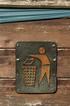 A metal litter sign screwed to a wooden bin showing a figure putting litter in a bin.