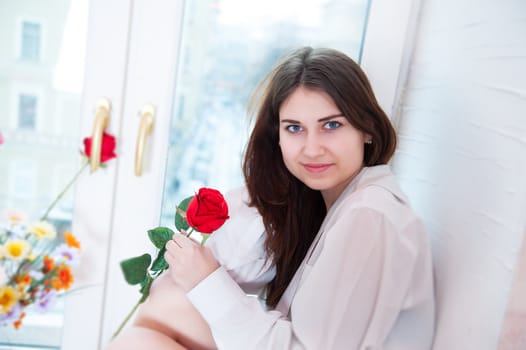 beautiful woman on the windowsill holding a red rose