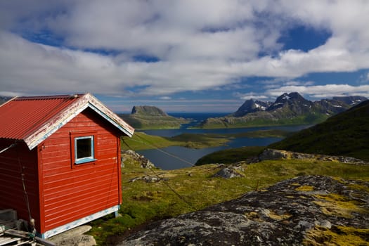 Picturesque panorama on Lofoten islands with red mountain cabin, fjords and high mountain peaks surrounding them