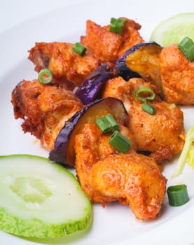 Grilled chicken on a white plate with vegetables on the background.