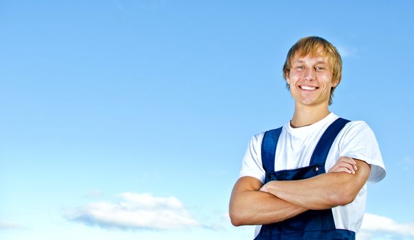 Smiling handyman in coveralls on sky background