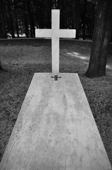 Cross and marble grave tombstone among trees.