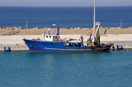 Fishing trawler in port. Rusty dragger ship tied to shore.