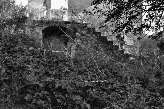 Man next to abandoned house obscured by overgrown plants. Black and white.