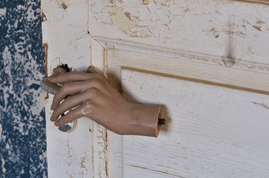 Detached mannequin doll hand pulling old door handle in haunted house.