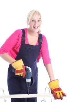 Happy woman in dungarees doing DIY renovations drilling a hole in a plank of wood isolated on white 