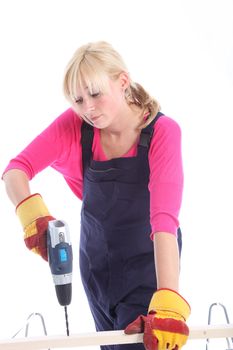 Woman in dungarees wearing protective gloves drilling a hole in a plank of wood isolated on white 