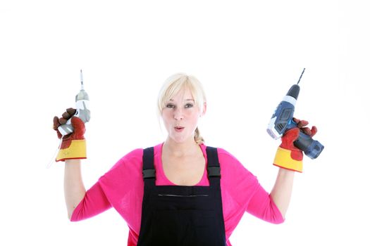 Laughing woman in dungarees holding up a mechanical screwdriver and portable handheld drill isolated on white 