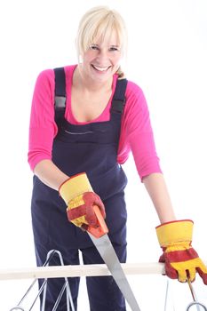 Happy woman dressed in dungarees and wearing protective gloves cutting timber with a handsaw 