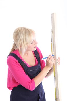 Woman in dungarees measuring and marking a length of wood isolated on white 