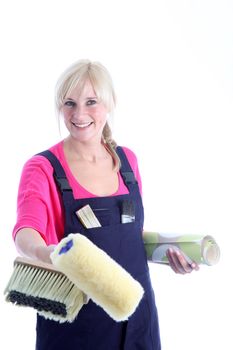Happy woman decorator in dungarees holding a roll of wallpaper, brush and roller as she embarks on a redecoration project Happy woman decorator in dungarees holding a roll of wallpeper, brush and roller as she embarks on a redecoration project 