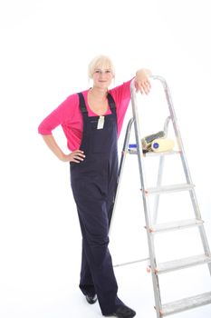 Attractive woman decorator in dungarees standing alongside a ladder and equipment ready to commence work on interior house decorating 