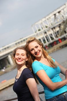 Two happy women friends standing back to back enjoying the summer sunshine on an urban waterfront 