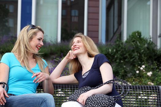 Two attractive young female friends chatting on a garden bench in the summer sunshine Two attractive young female friends chatting on a garden bench in the summer sunshine