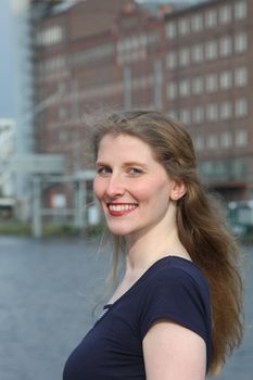 Smiling self-assured mature woman standing sideways looking over her shoulder at the camera in an urban environment with copyspace 