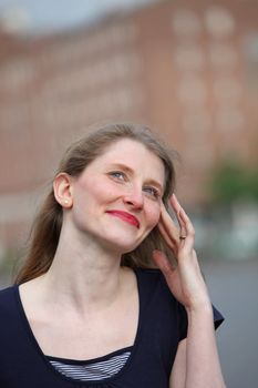 Smiling graceful woman with her fingertips to her temple and her eyes raised to the sky in an urban environment 