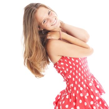 Happy carefree teenage girl in a trendy red and white polka dot dress smiling vivaciously as she flicks her long blonde hair 