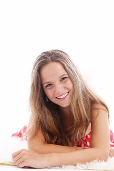 Happy young teenager with a vivacious smile relaxing on a carpet lying on her stomach looking at the camera 