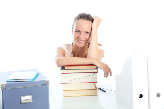Beautiful young teenage student with a happy smile seated at her desk leaning on a large pile of textbooks for her studies