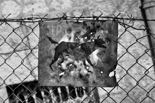 Beware of the dog rusty sign and barbed wire fence. Black and white.