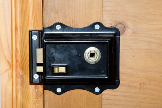 A vintage metal lock painted black with brass levers and dead lock mounted on a stripped wood door.