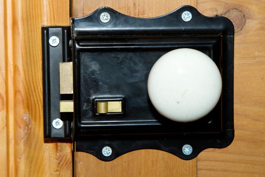 A vintage metal lock and white china knob, painted black with brass levers and dead lock mounted on a stripped wood door.