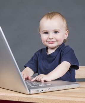 young child with laptop computer on wooden desk in grey background