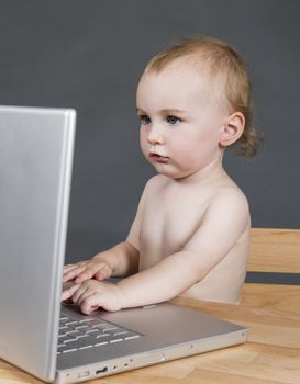 young child with laptop computer on wooden desk in grey background