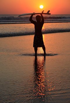 Silhouette of surfer at red sunset. Kuta beach. Bali