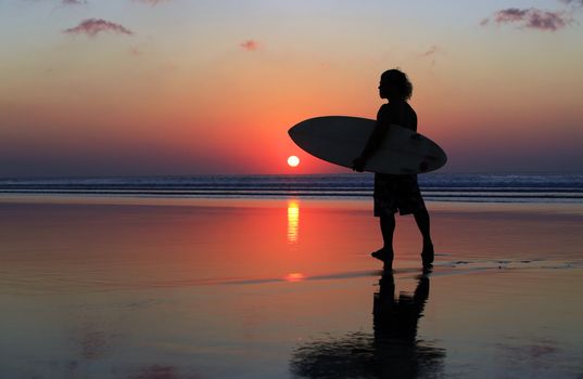 Silhouette of surfer at red sunset. Kuta beach. Bali