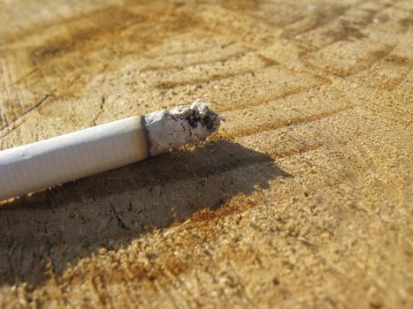 A fuming cigarette lays on the wooden surface