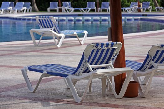 Resort pool lounge chairs sitting beside a large pool.