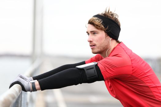 Male runner stretching after running in cold fall weather wearing warm sporty running clothing. Handsome male fitness sport model outdoors.