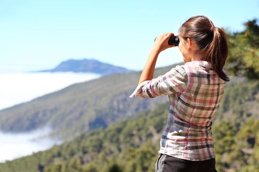 Hiker looking in binoculars enjoying view above clouds during hiking trip. Young Asian woman on hike on La Palma, Canary Islands, Spain.