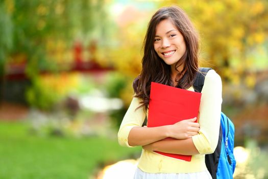 Beautiful woman holding red book in autumn background. Asian student girl on campus