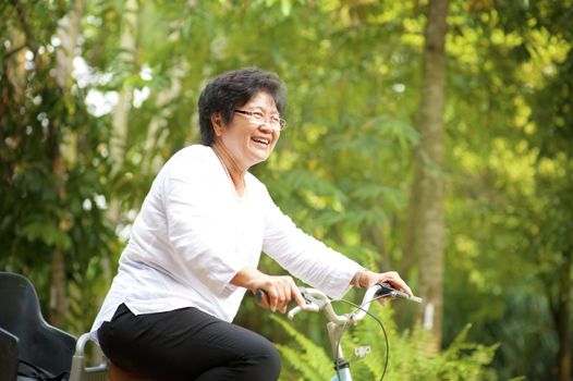 60s senior Asian woman riding on bicycle outdoor with great fun