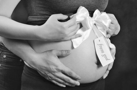 Pregnant woman and husband hand on stomach with ribbon and tag