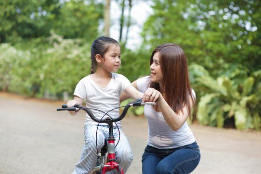 Asian mother teaching little girl to ride a bike