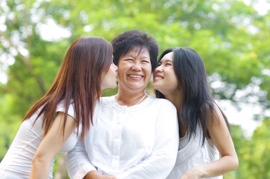 Young Asian daughter kissing their senior mother, outdoor park