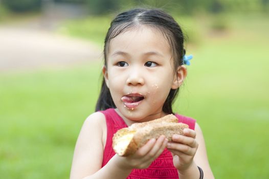 Little Asian girl eats a sandwich and licking lips on fresh air